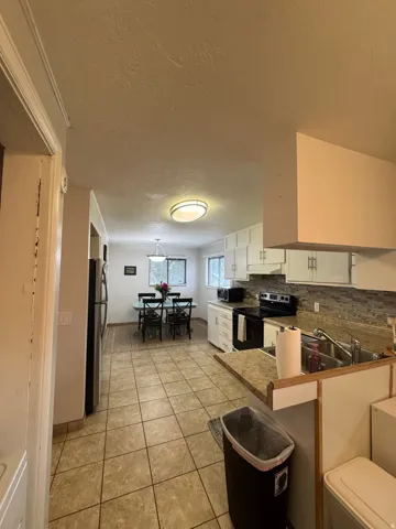 Kitchen featuring tile flooring, white cabinetry, integrated stainless steel sink, and a tiled backsplash