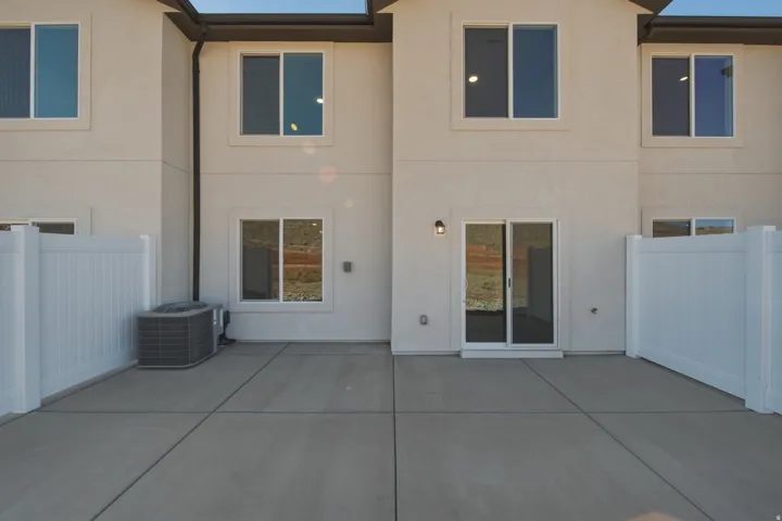 Concrete patio, white vinyl fencing, sliding glass door, and exterior sconce lighting