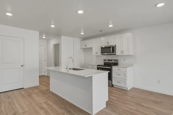 Kitchen featuring an island with an integrated sink and gooseneck faucet, white shaker-style cabinetry, stainless steel appliances, and light-colored countertops