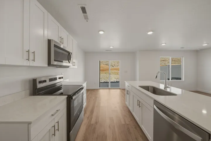 White shaker-style cabinetry with stainless steel hardware, stainless steel appliances, light-toned wood-finish flooring, recessed lighting, and a kitchen island with an undermount sink