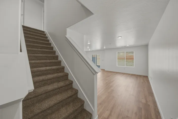 Carpeted staircase with white railing, wood-finish flooring, recessed lighting, and a sliding glass door