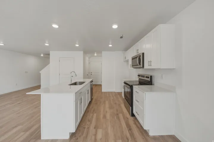 Open-concept kitchen with white cabinetry, stainless steel appliances, a center island with a sink, and wood-finish flooring