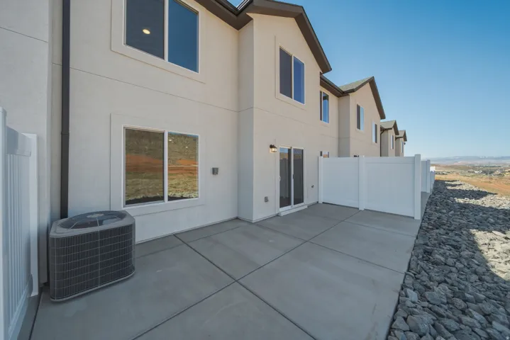 Rear patio featuring a concrete slab, white vinyl fencing, and an exterior light fixture