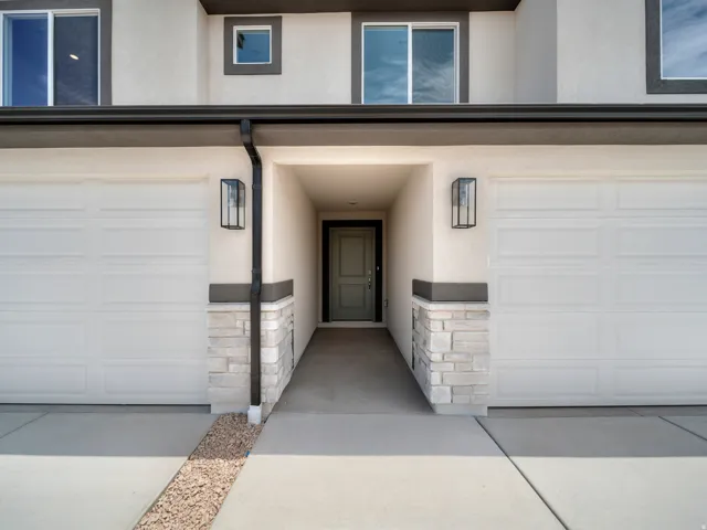 Two single-panel garage doors, light-colored stacked stone detailing, and exterior wall sconces flank the main entry