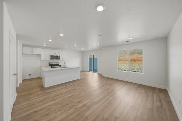 Open-concept living space with wood-finish flooring, recessed lighting, and a kitchen island featuring a stainless steel sink