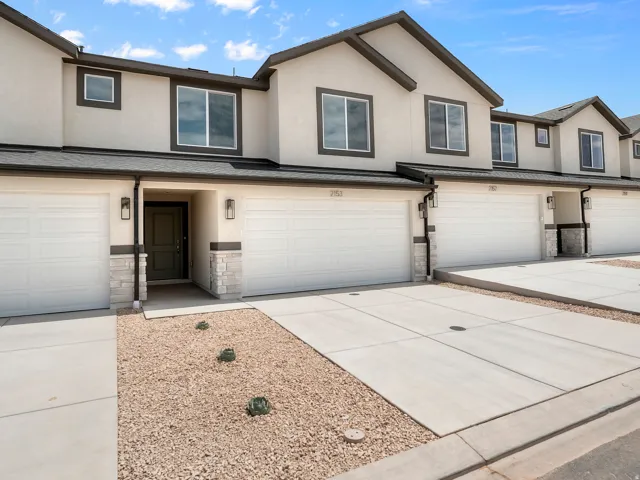 Stucco exterior with dark trim accents, attached garages, stone veneer detailing, concrete driveways, and drought-tolerant landscaping
