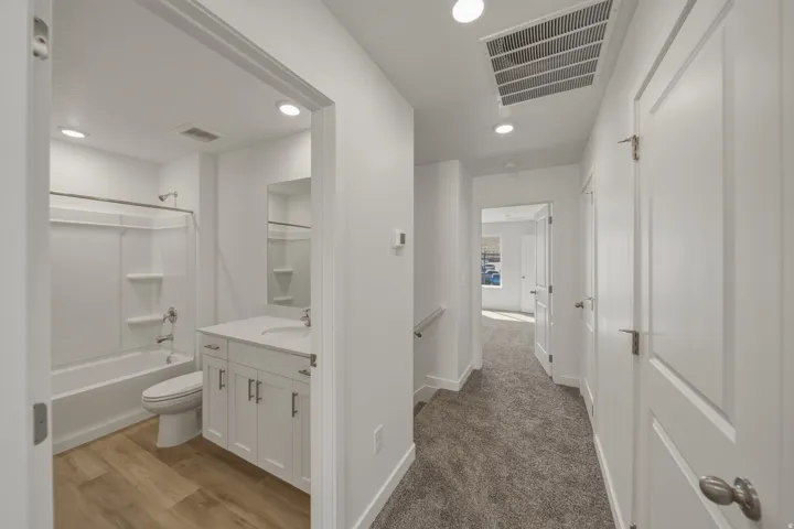 Bathroom featuring a white vanity with integrated sink, white tub/shower combination, and wood-finish flooring