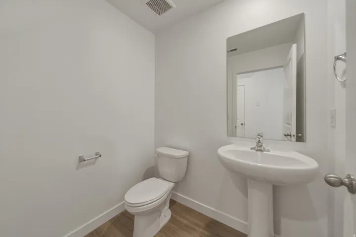 Pedestal sink with chrome faucet, wall-mounted mirror, toilet, and wood-finish flooring