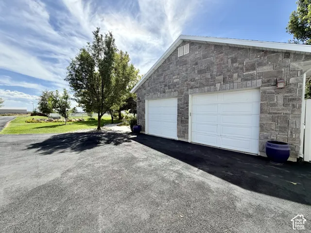 Stone-clad exterior featuring two garage doors, an exterior wall light, a white gable vent, and a paved driveway