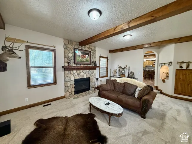 Stone-faced fireplace with a wood mantel, wood-framed windows, and decorative ceiling beams