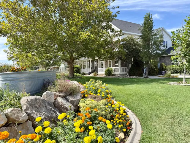 Manicured lawn with a curved paver border, vibrant floral landscaping, rock garden, and a galvanized raised garden bed
