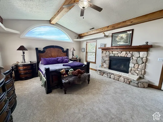 Floor-to-ceiling river rock fireplace with an expansive hearth, vaulted ceiling with exposed wood beams, arch-top window, and ceiling fan