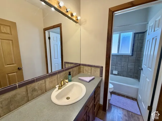 Wood-finish vanity with an integrated sink and brass-finish faucet, featuring a tiled backsplash and overhead lighting
