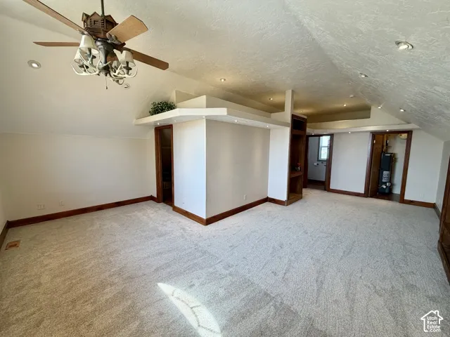 Spacious carpeted room featuring vaulted ceilings, recessed lighting, a ceiling fan with integrated lighting, and rich wood-toned built-in shelving