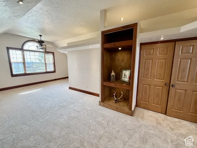 Built-in wood shelving with integrated lighting, wood-finish doors, arched window with wood trim, ceiling fan, and recessed lighting