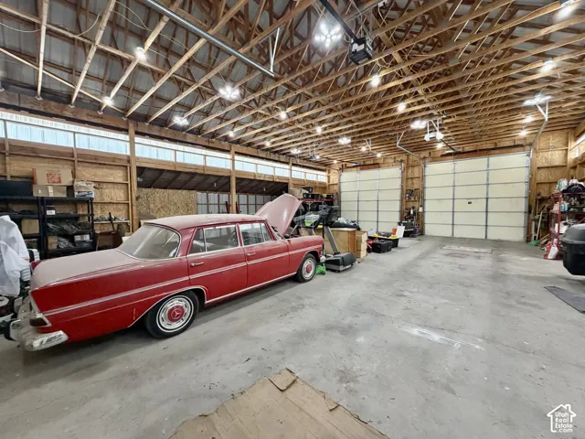 Spacious interior with exposed wood beam ceiling, concrete flooring, multiple overhead lights, and two large garage doors