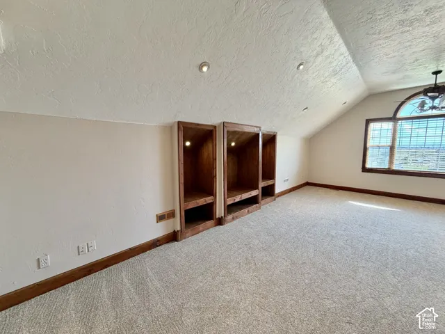 Angled ceiling with recessed lighting, three built-in wood-finish shelving units, arched window, ceiling fan, and light-colored carpeting