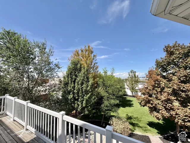 Balcony with white railing and wood-finish decking overlooking a spacious lawn and mature trees