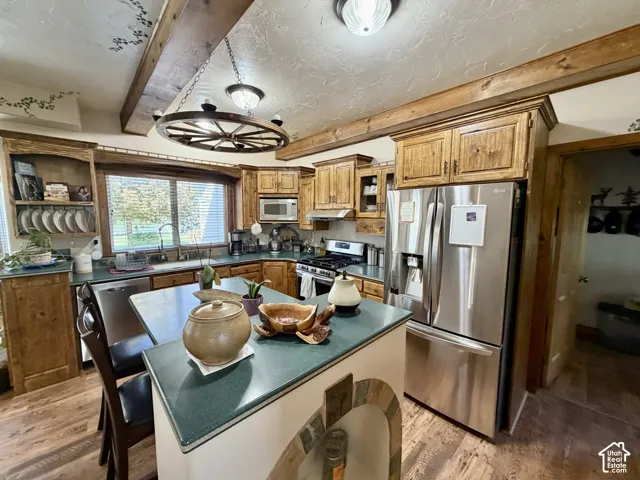 Kitchen featuring wood-finish flooring, exposed ceiling beams, stainless steel appliances, and a built-in kitchen island with seating