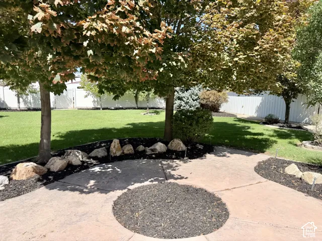 Expansive lawn with mature trees, a stamped concrete patio, decorative rock landscaping, and a privacy fence