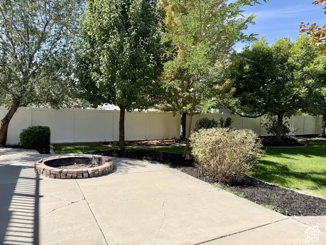 Patio with a built-in stone fire pit, surrounded by mature trees, landscaping, and a privacy fence
