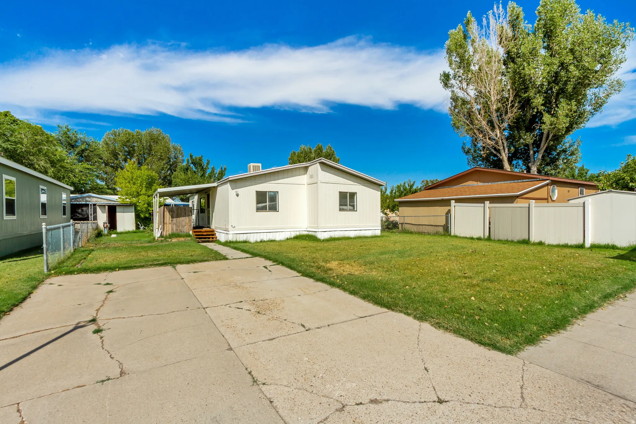 Expansive concrete driveway, manicured lawn, and a light-colored exterior finish