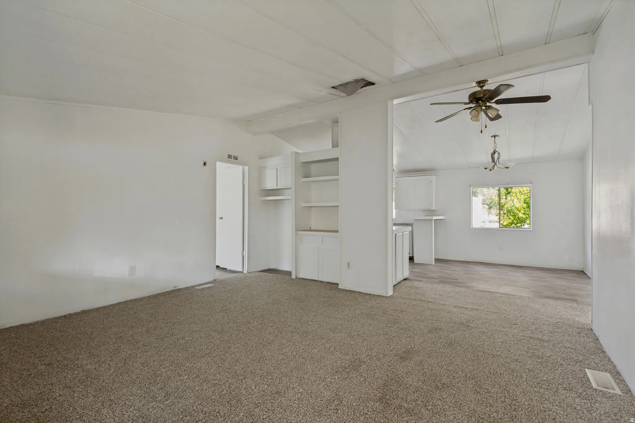 Open concept living area with carpeting, built-in shelving, a ceiling fan, and wood-finish flooring in the dining area
