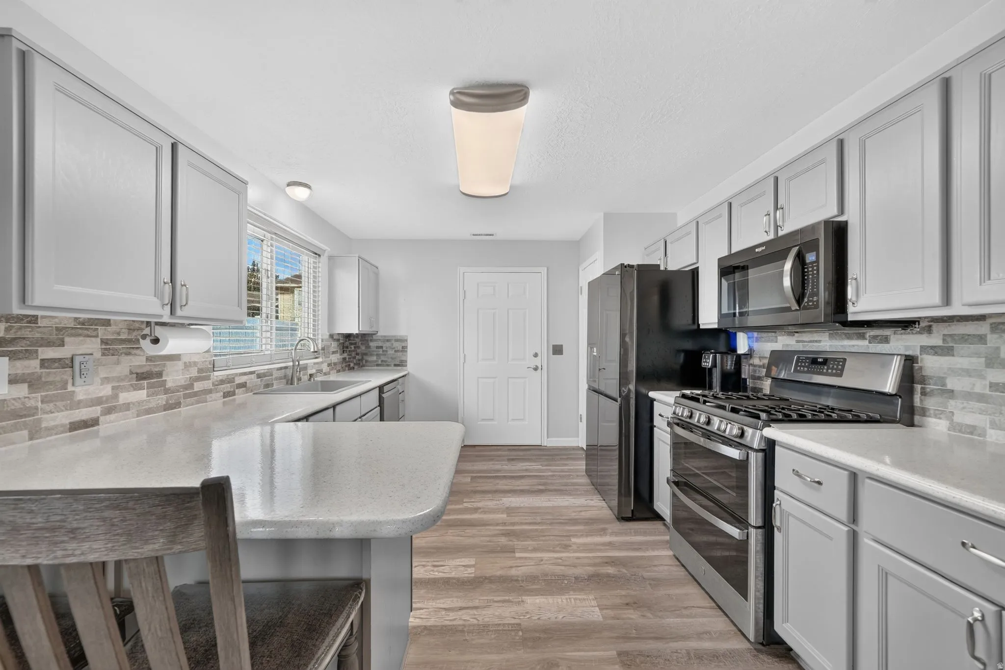 Kitchen featuring light gray cabinetry, light-toned countertops, a multi-tone tile backsplash, and wood-finish flooring