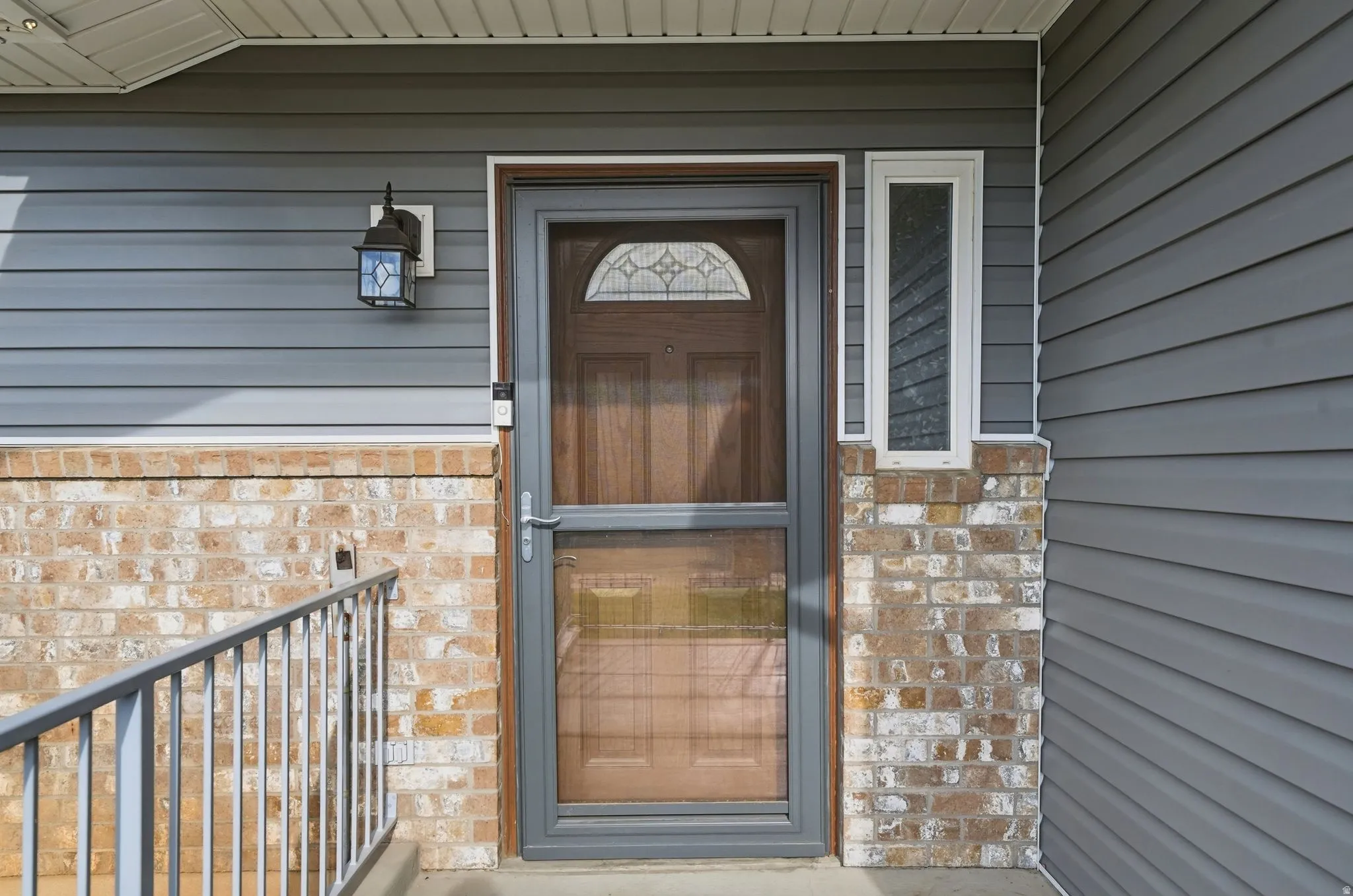 Welcoming entry featuring a wood-finish door with transom window detail, framed by a gray composite frame and sidelite