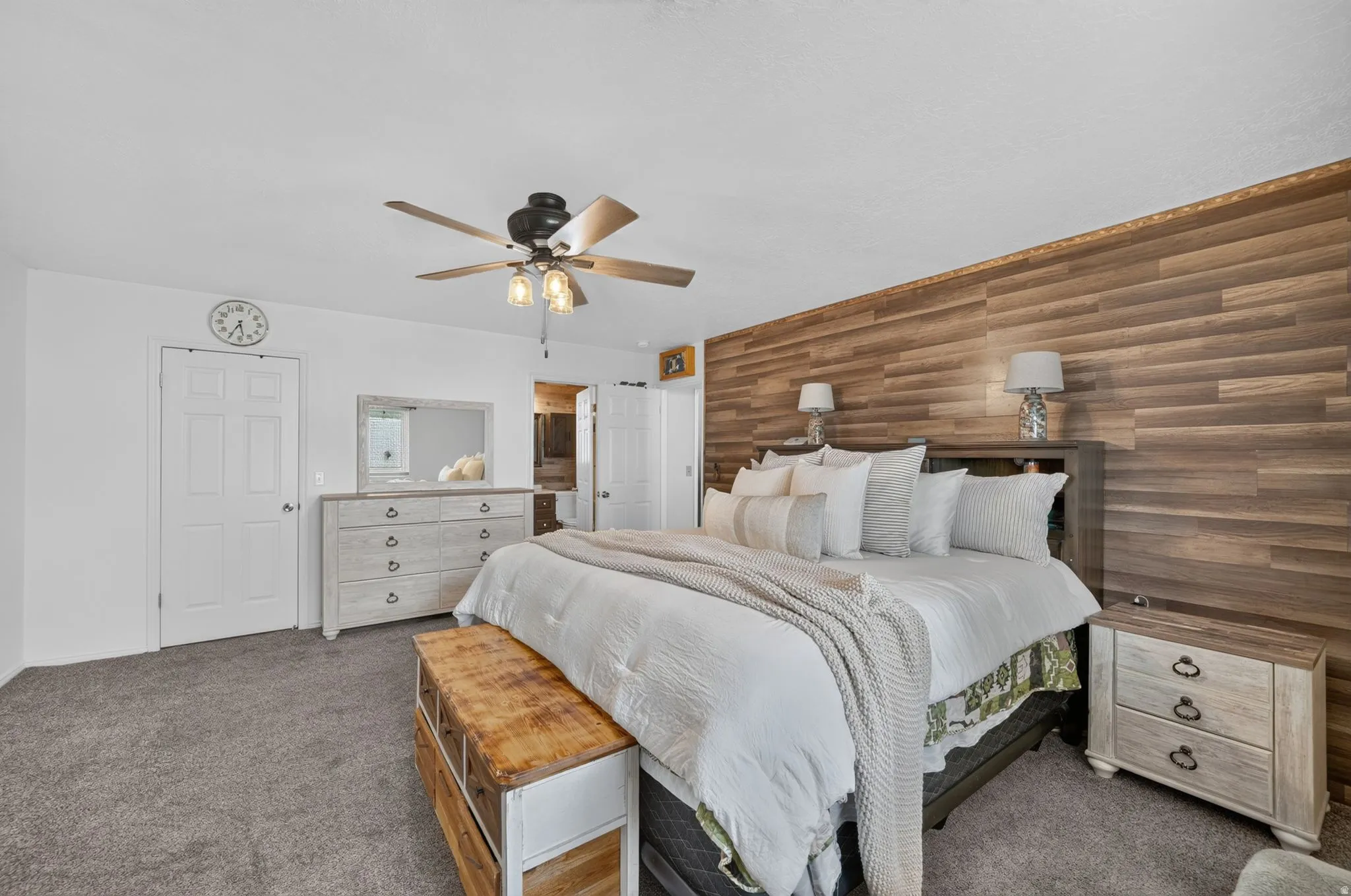 Wood-finish accent wall, ceiling fan with integrated lighting, two panel doors, and grey carpeting