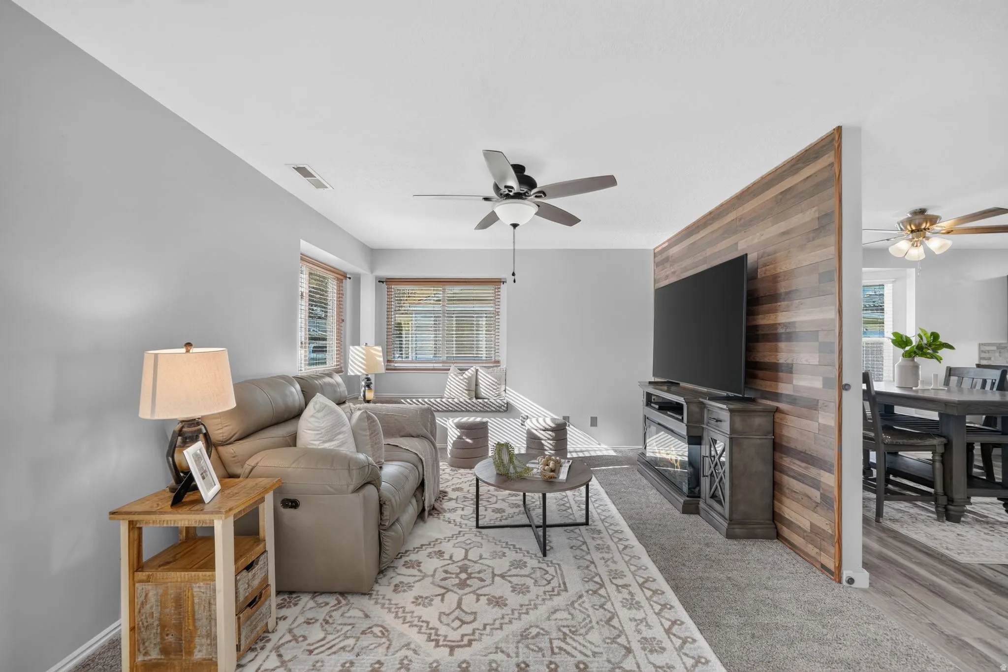 Accent wall with wood-look paneling, ceiling fan with light fixture, window with blinds, window seat, and wood-finish flooring