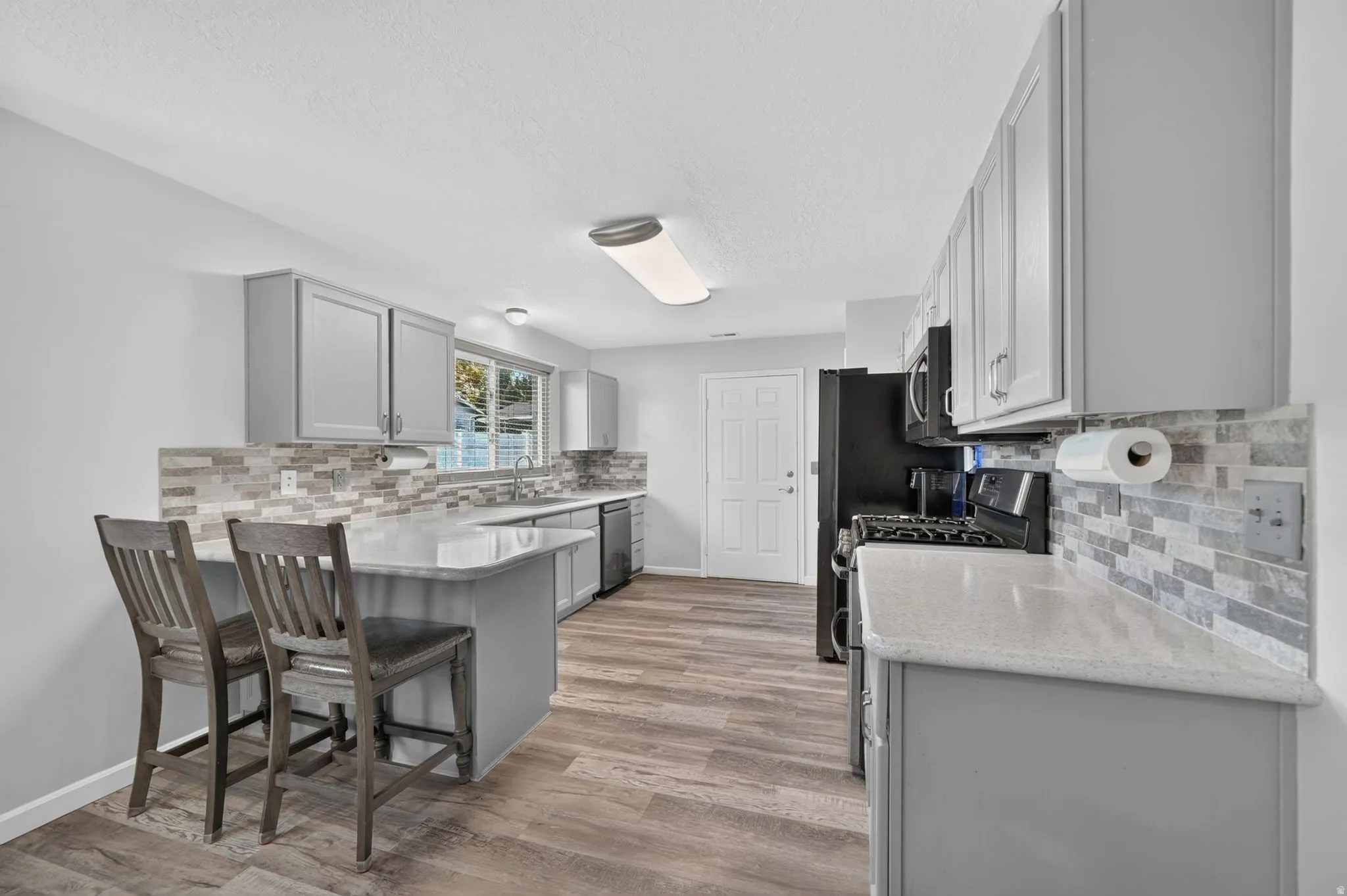 Renovated kitchen featuring gray cabinetry, quartz countertops, subway tile backsplash, and stainless steel appliances including a gas range