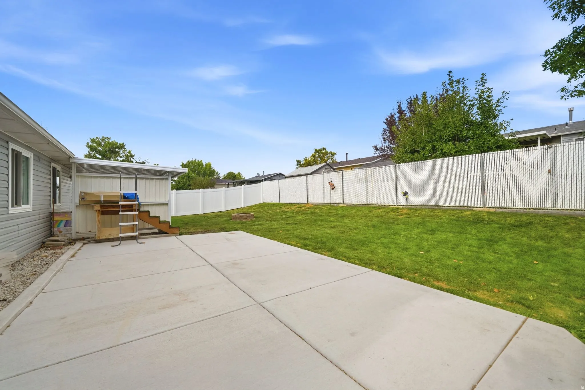 Expansive concrete patio with clean, geometric seams opening to a level, manicured lawn bordered by a white vinyl privacy fence