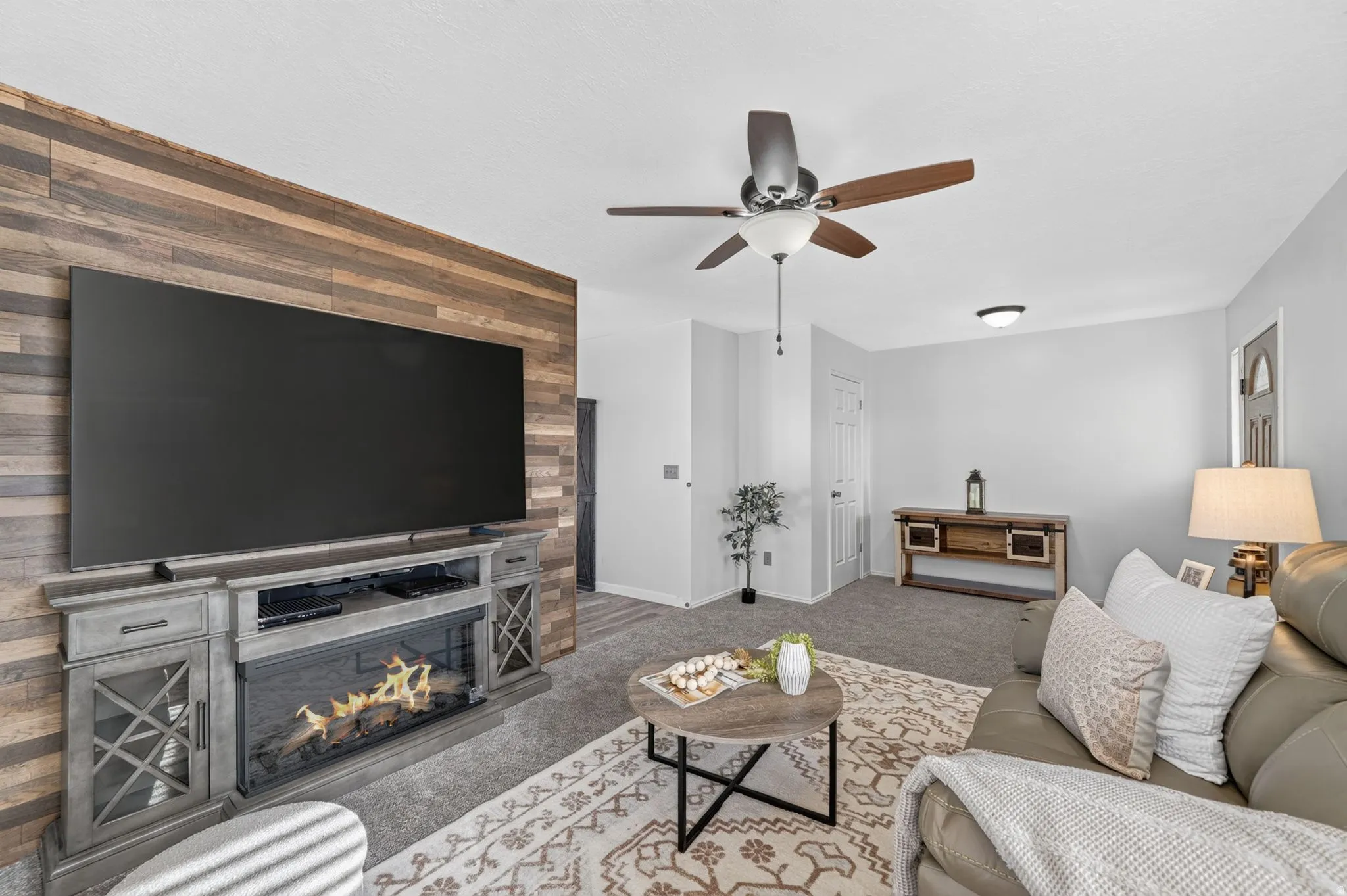 Spacious living room featuring a wood-finish accent wall with a gas fireplace insert and built-in cabinetry, a flat-screen television mounted above, ceiling fan with brushed metal finish, recessed lighting, and neutral upholstered seating arranged around