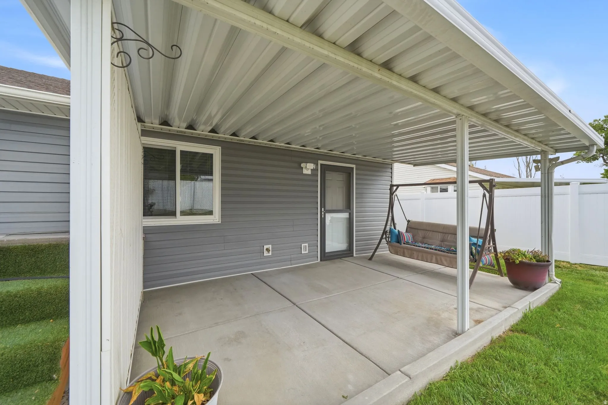 Covered patio with corrugated metal roof and white support columns, concrete flooring, and direct access to the home via glass door