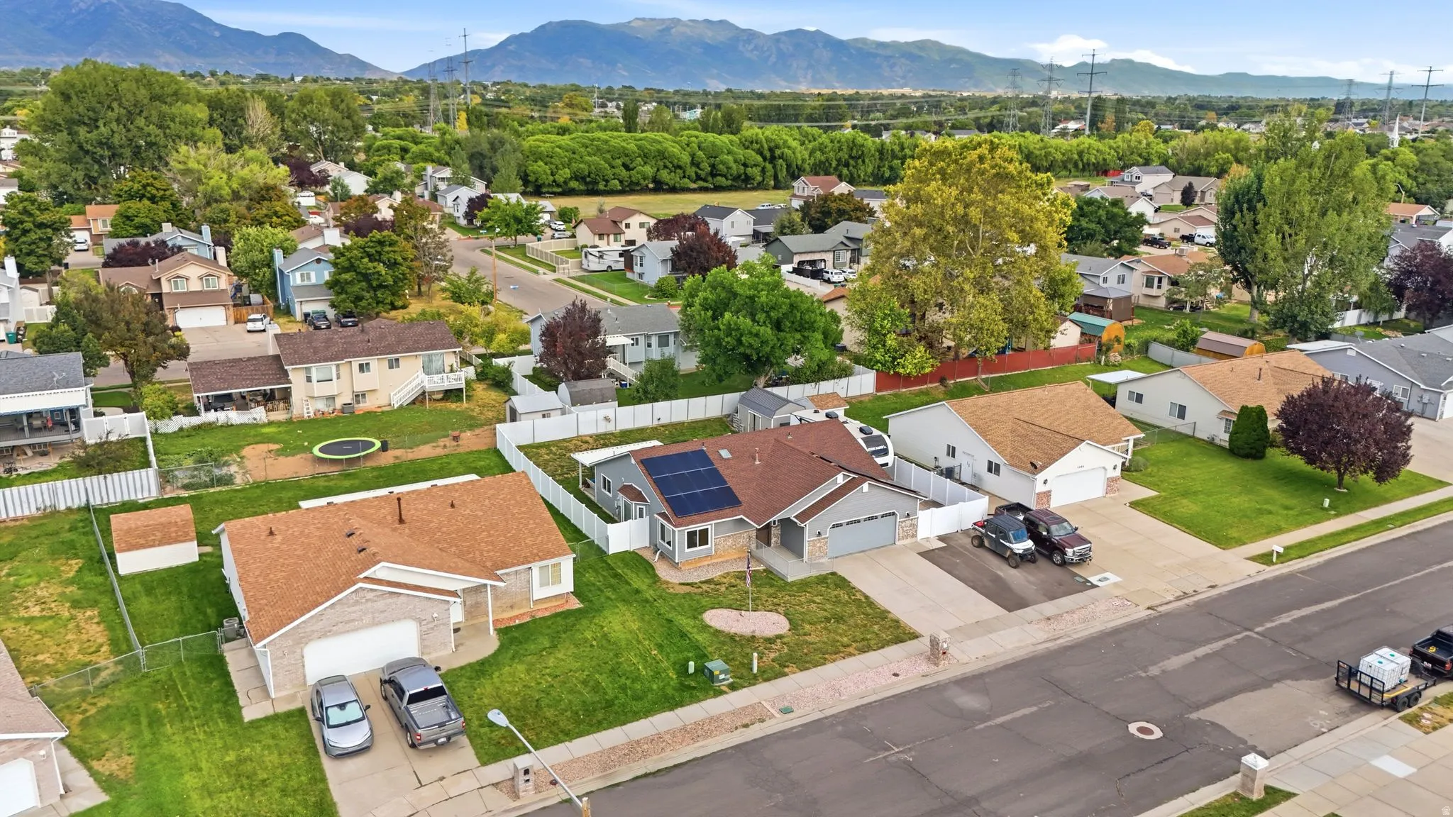 Aerial view showcasing a single-story residence with a clay tile roof, situated on a generous corner lot with mature landscaping and established trees