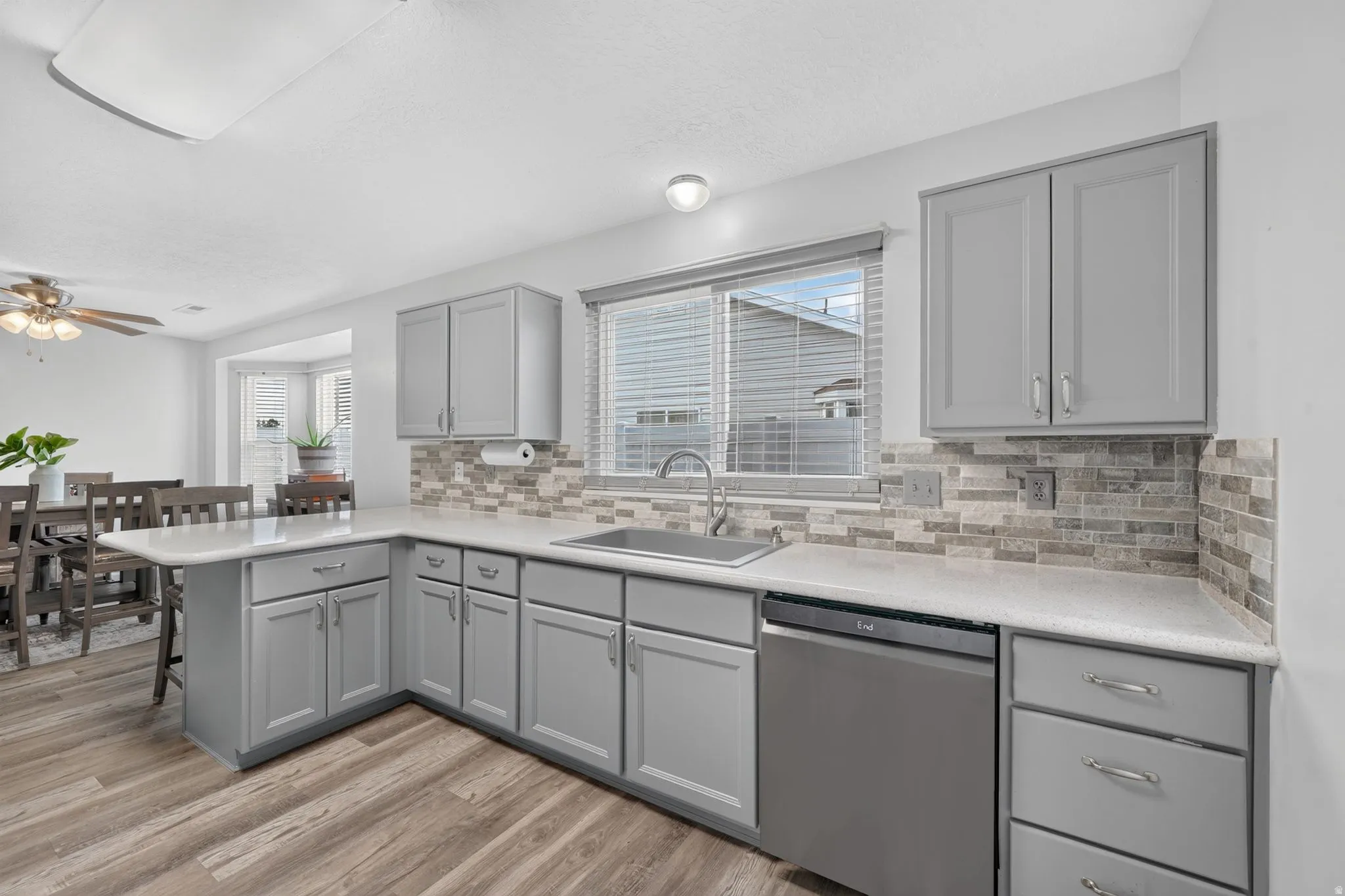 Kitchen featuring light gray cabinetry, light-colored countertops, a stainless steel sink, a stainless steel dishwasher, and wood-finish flooring
