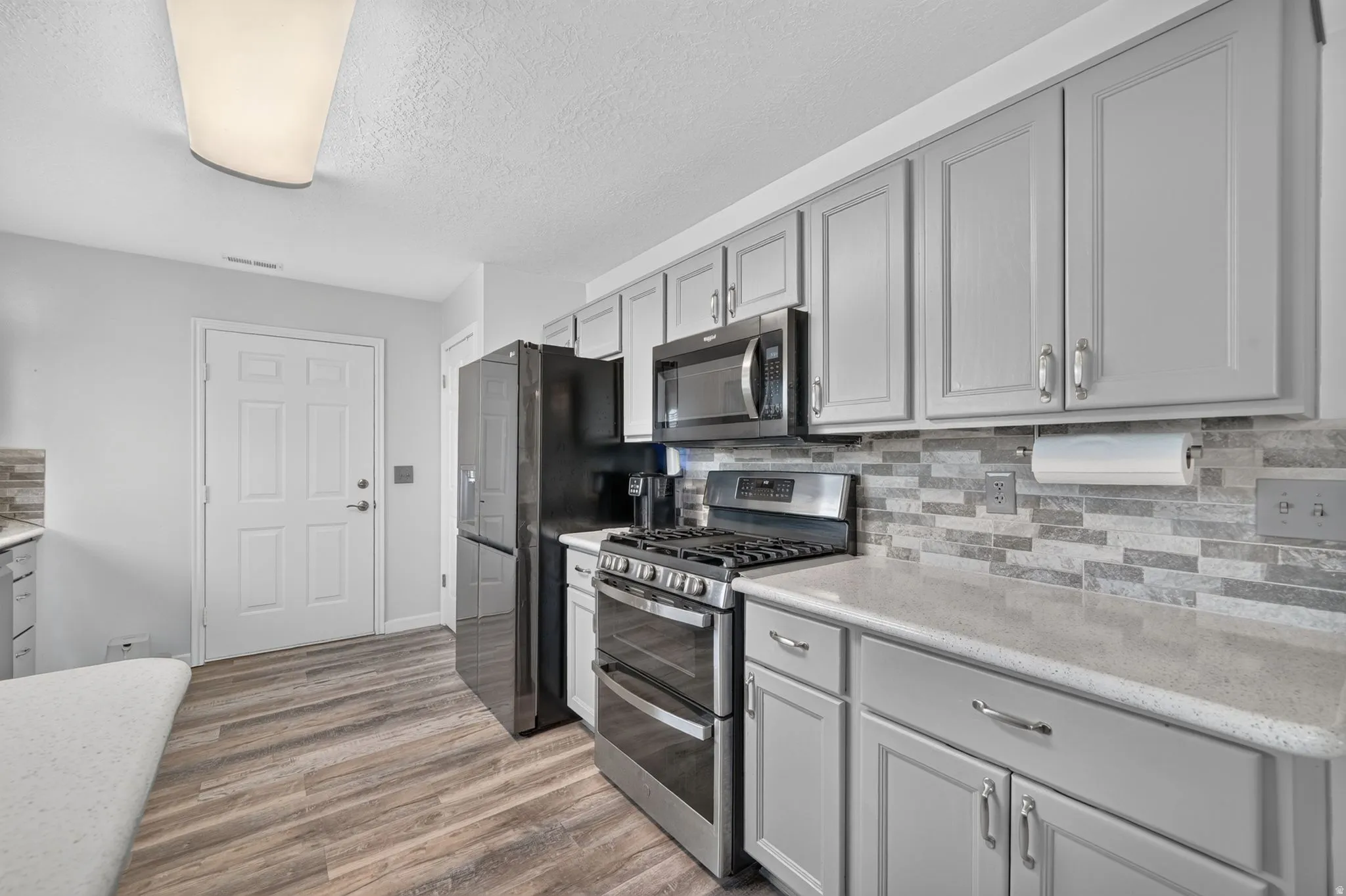 Updated kitchen featuring white cabinetry with hardware accents, stainless steel appliances including a gas range and microwave, subway tile backsplash, quartz countertops, and wood-finish flooring throughout the space