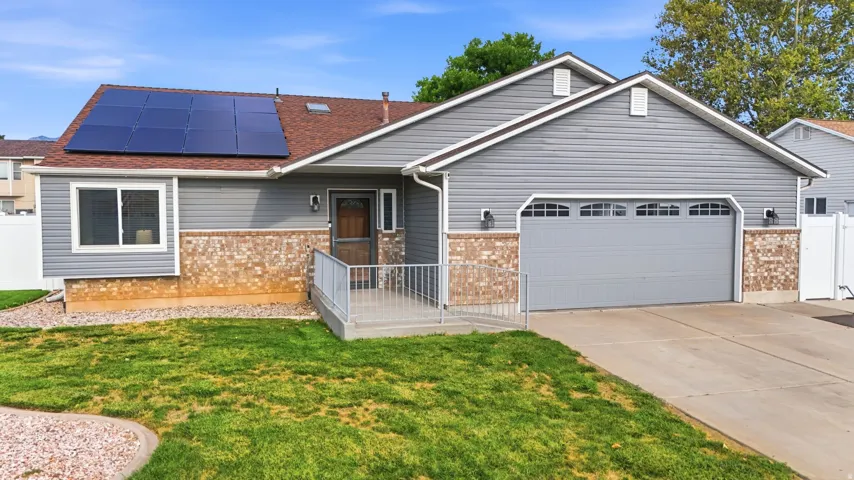 Modern ranch-style home featuring a freshly finished exterior with brick and siding accents, a two-car garage with paneled doors, a covered front porch with metal railings, mature landscaping with manicured lawn and established trees, and solar panel arra