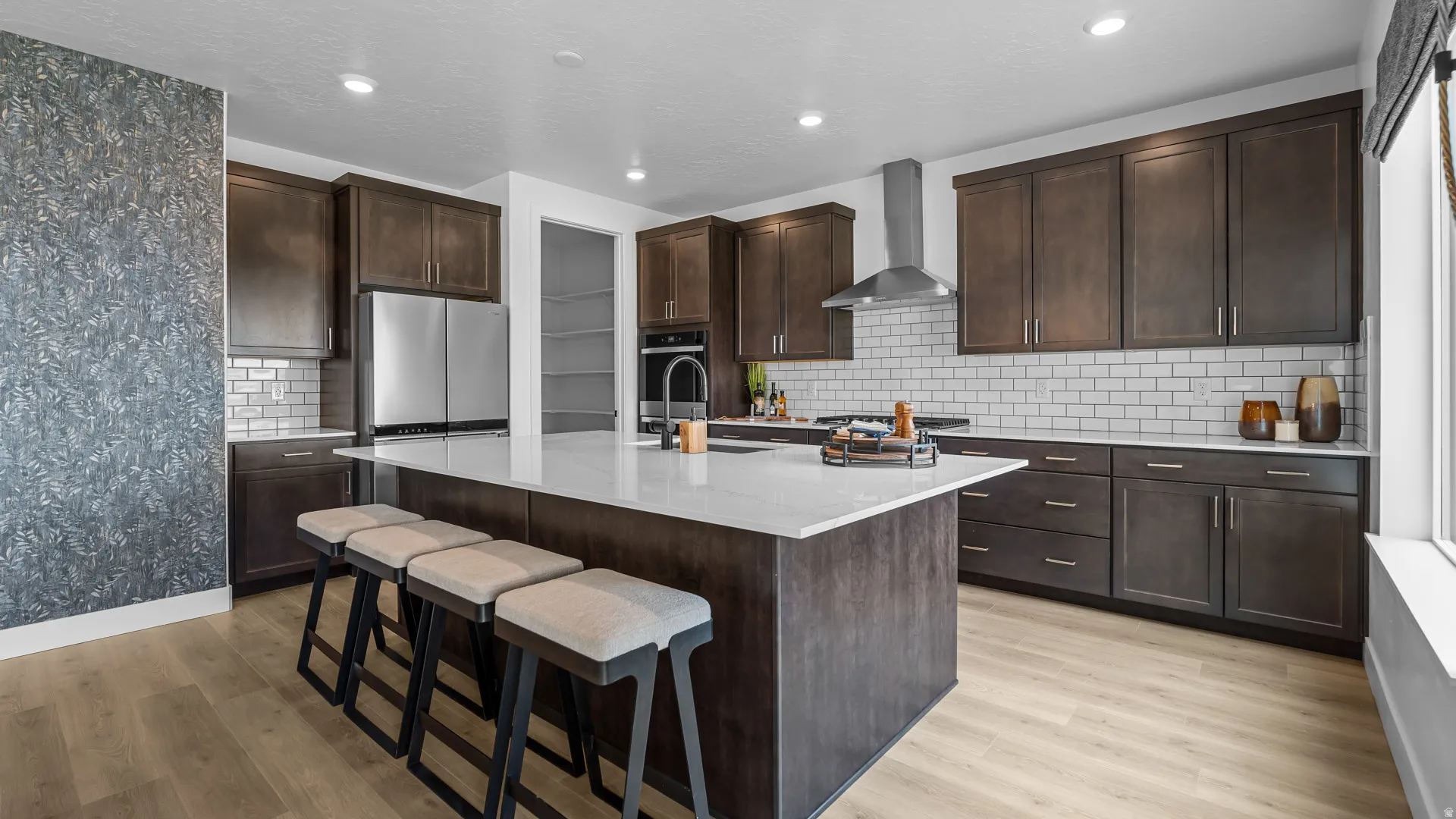 Spacious kitchen featuring an expansive center island, dark wood-finish cabinetry, stainless steel appliances, white subway tile backsplash, and light wood-finish flooring