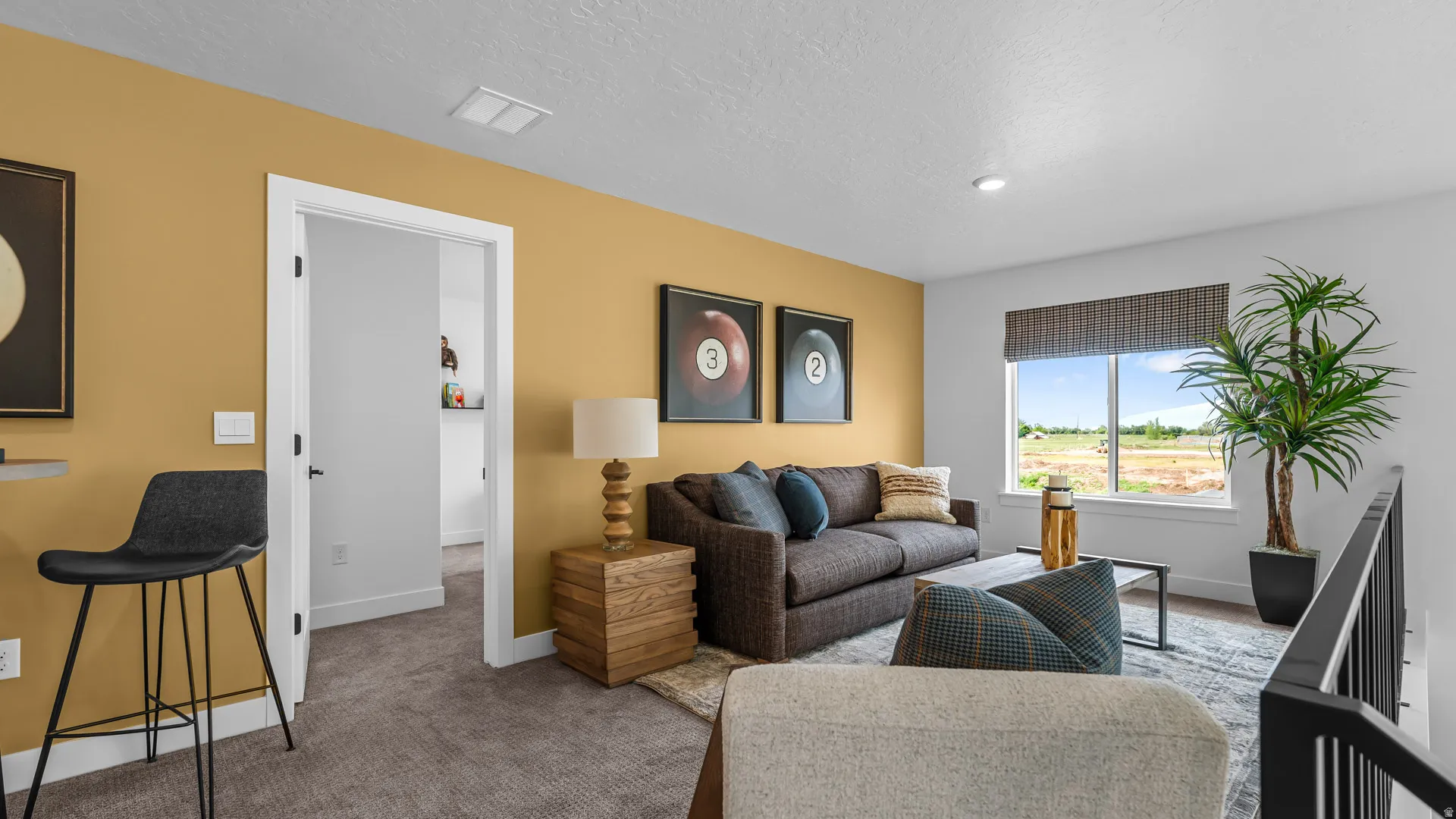 Carpeted flooring, white trim, open doorway, window with blinds, and black metal railing