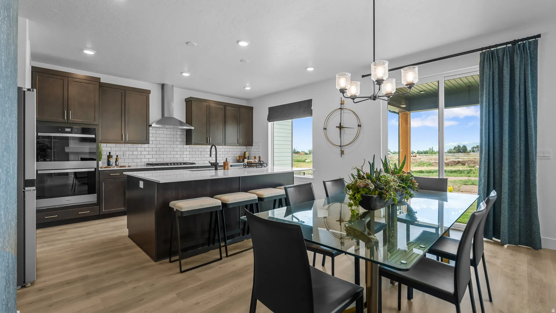 Modern kitchen featuring dark wood cabinetry, white subway tile backsplash, stainless steel appliances, a center island with countertop seating, and light wood-finish flooring