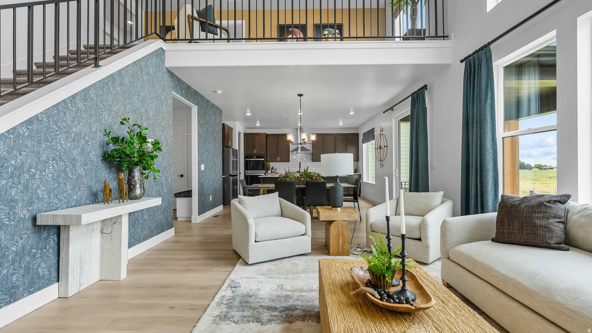 Open-concept living area with high ceilings, light wood-finish flooring, and a second-story overlook with metal railing