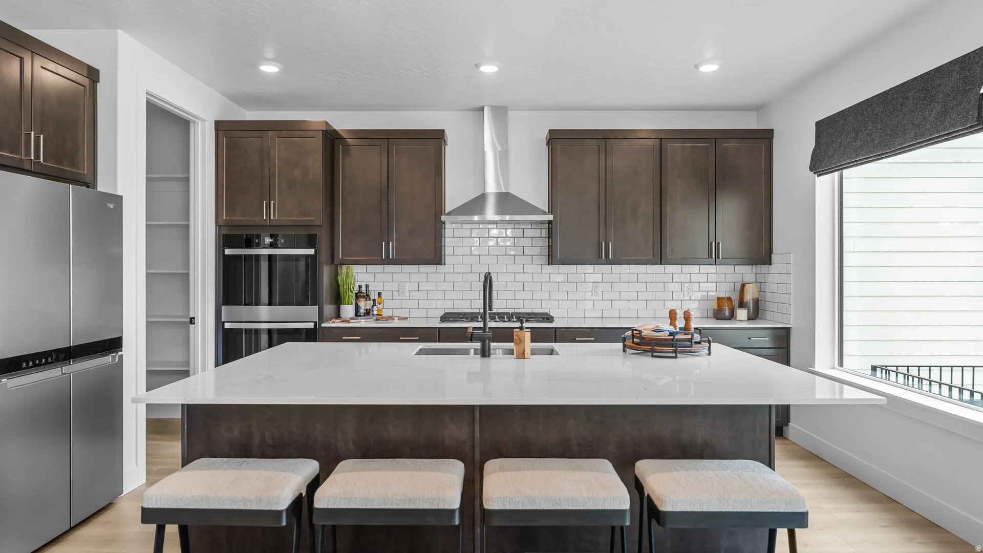 Gourmet kitchen featuring a large central island with seating, stainless steel appliances, dark wood cabinetry, and white subway tile backsplash