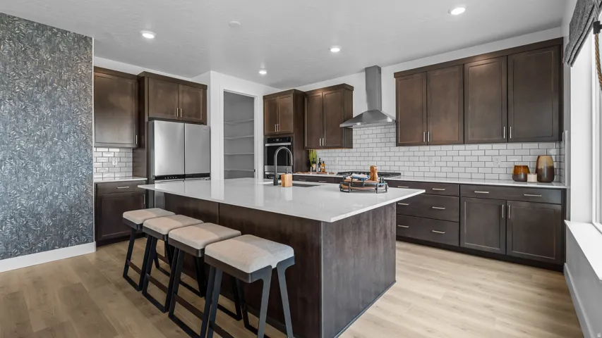 Spacious kitchen featuring an expansive center island, dark wood-finish cabinetry, stainless steel appliances, white subway tile backsplash, and light wood-finish flooring