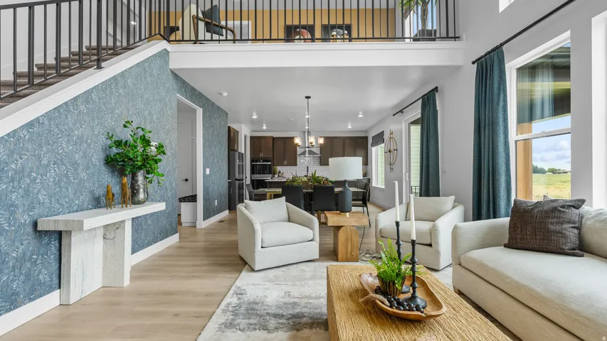 Open-concept living area with high ceilings, light wood-finish flooring, and a second-story overlook with metal railing