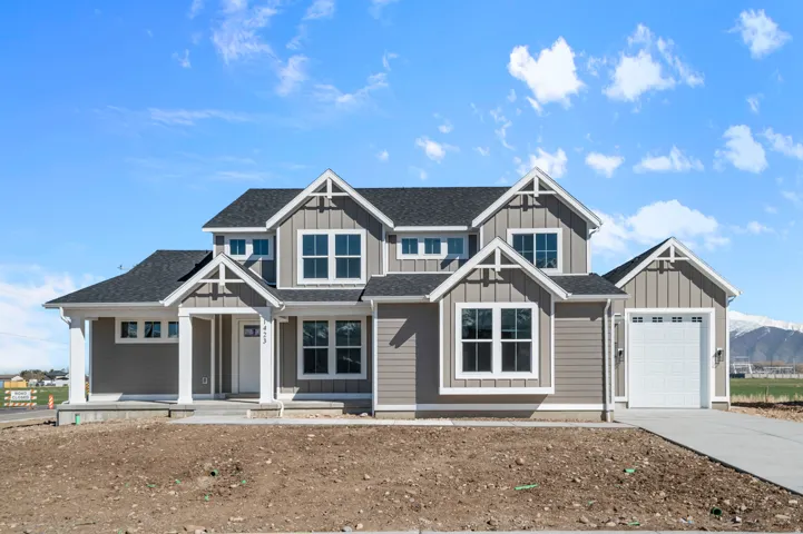 Gray siding exterior with white trim, covered front porch, attached garage with a white door, concrete driveway, and dark shingle roof