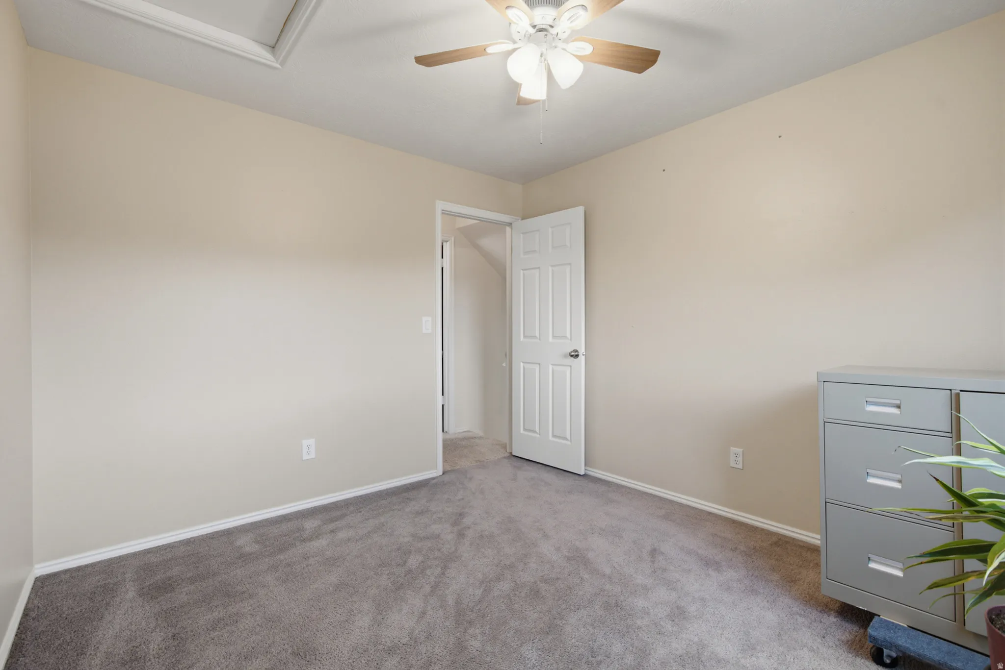 Neutral tone wall paint, textured carpet flooring, ceiling-mounted fan with light fixture, and white trim work