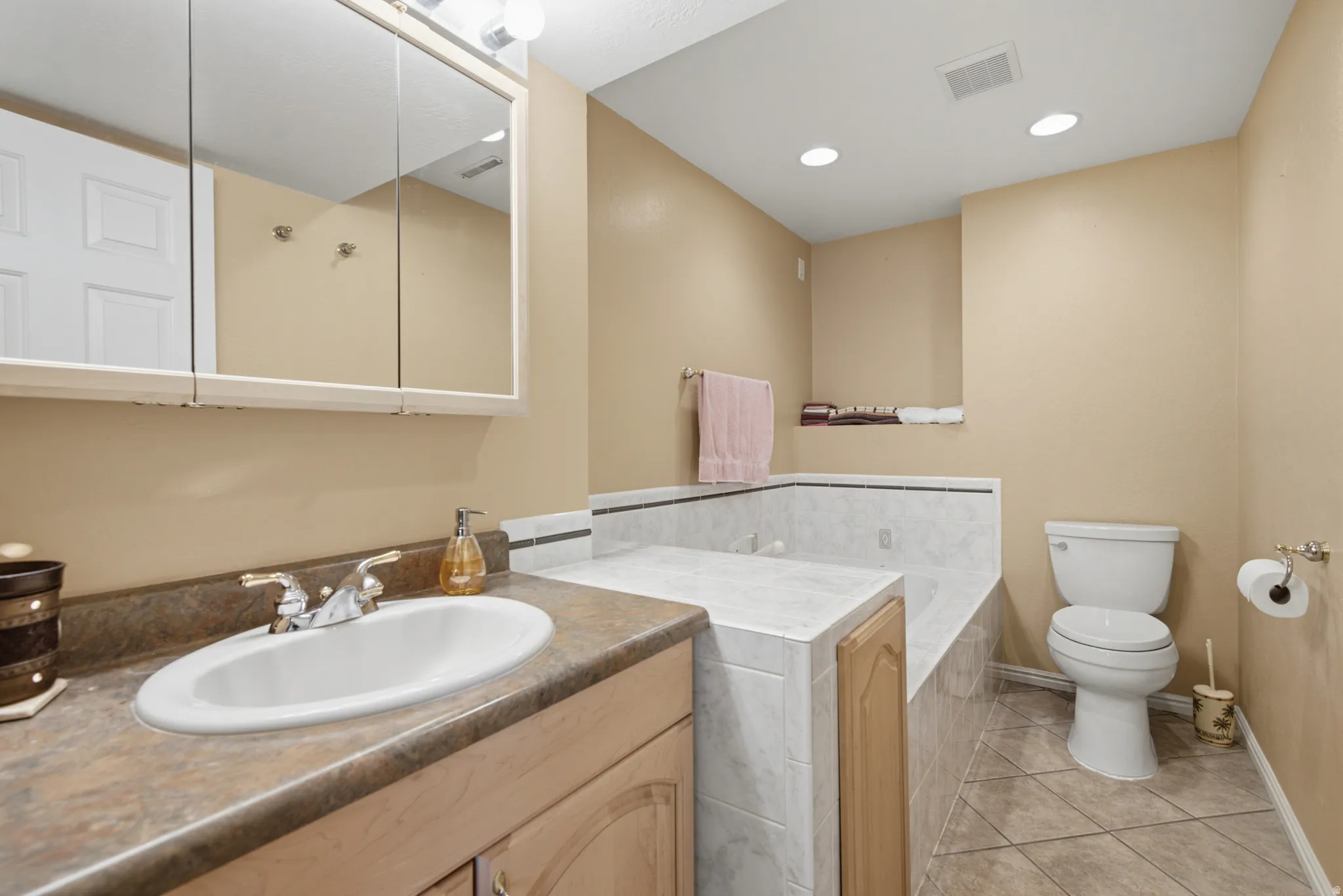 Vanity with integrated sink, medicine cabinet with mirrored doors, tiled jetted bathtub, tiled flooring, and recessed ceiling lighting