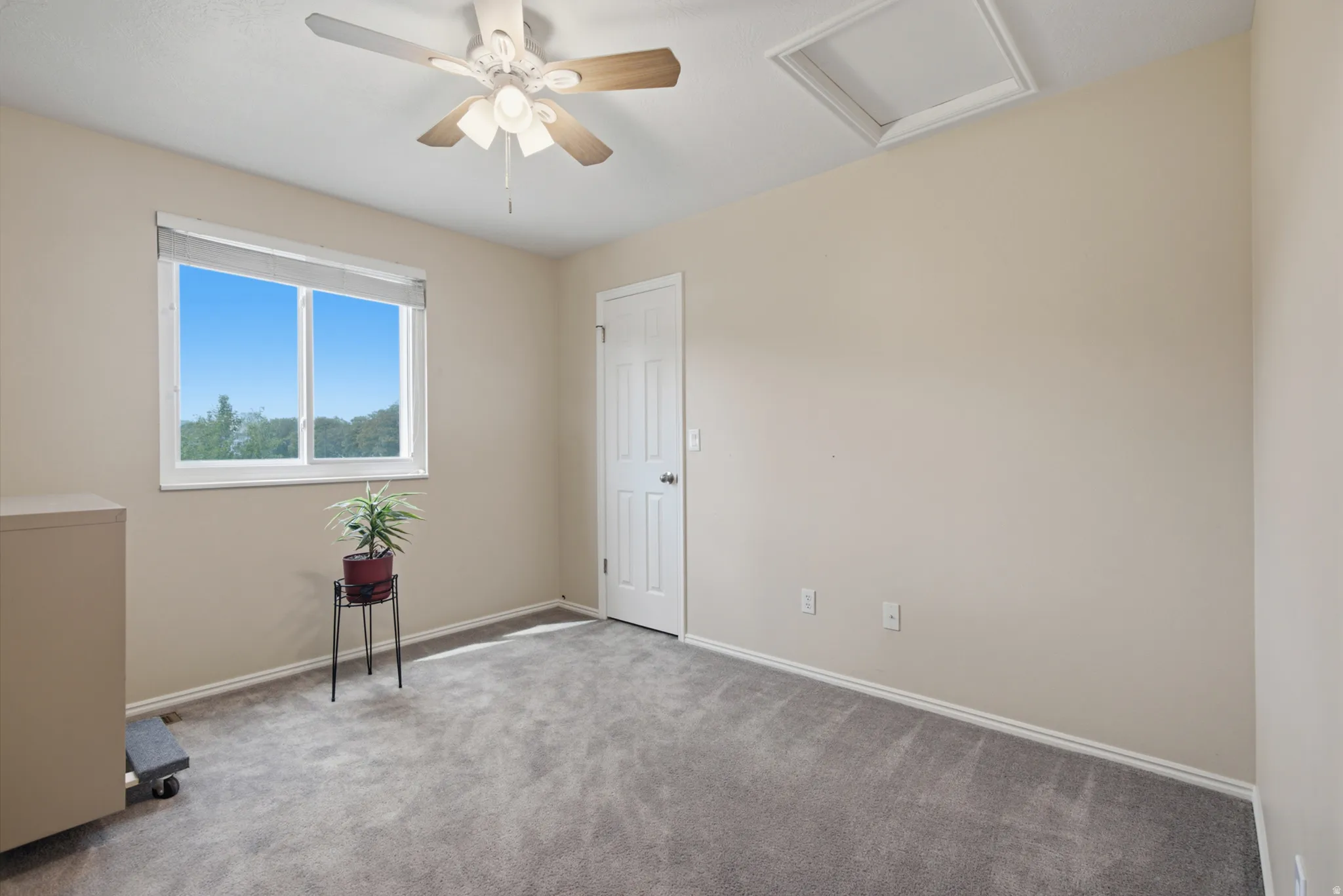 Room featuring neutral wall tones, gray carpeting, a window with a blue sky backdrop, and a ceiling fan with integrated lighting